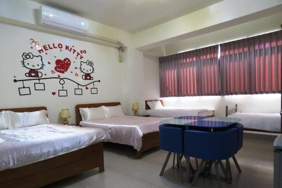 Hotellihuone, jossa on kaksi sänkyä, pieni pöytä ja Hello Kitty -aiheinen seinäkoriste.