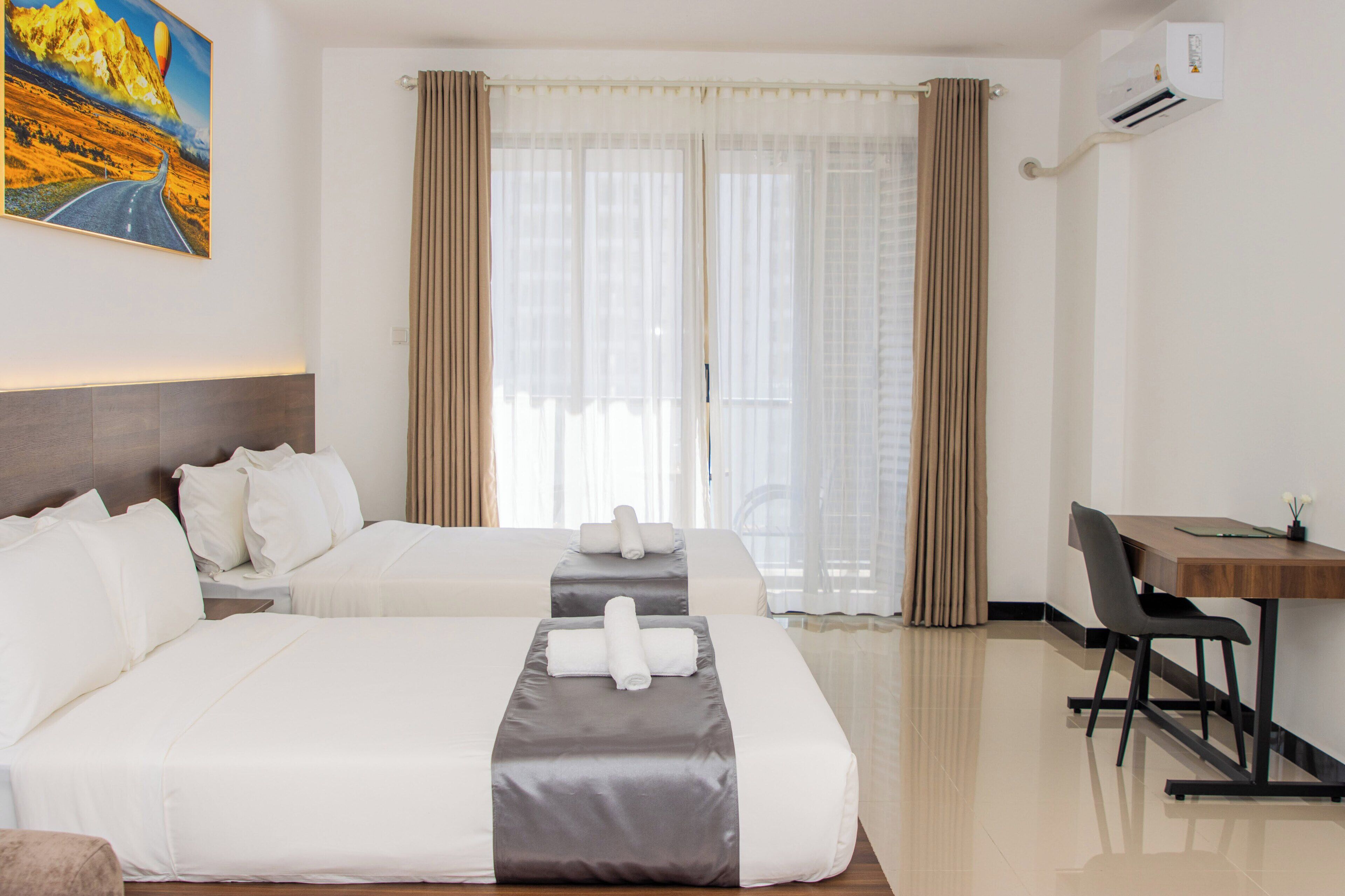 A hotel room with two beds, a desk, and a window with curtains.