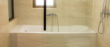 Une salle de bain moderne dotée d’une baignoire sur pieds, d’un espace douche et d’une fenêtre laissant entrer la lumière naturelle.