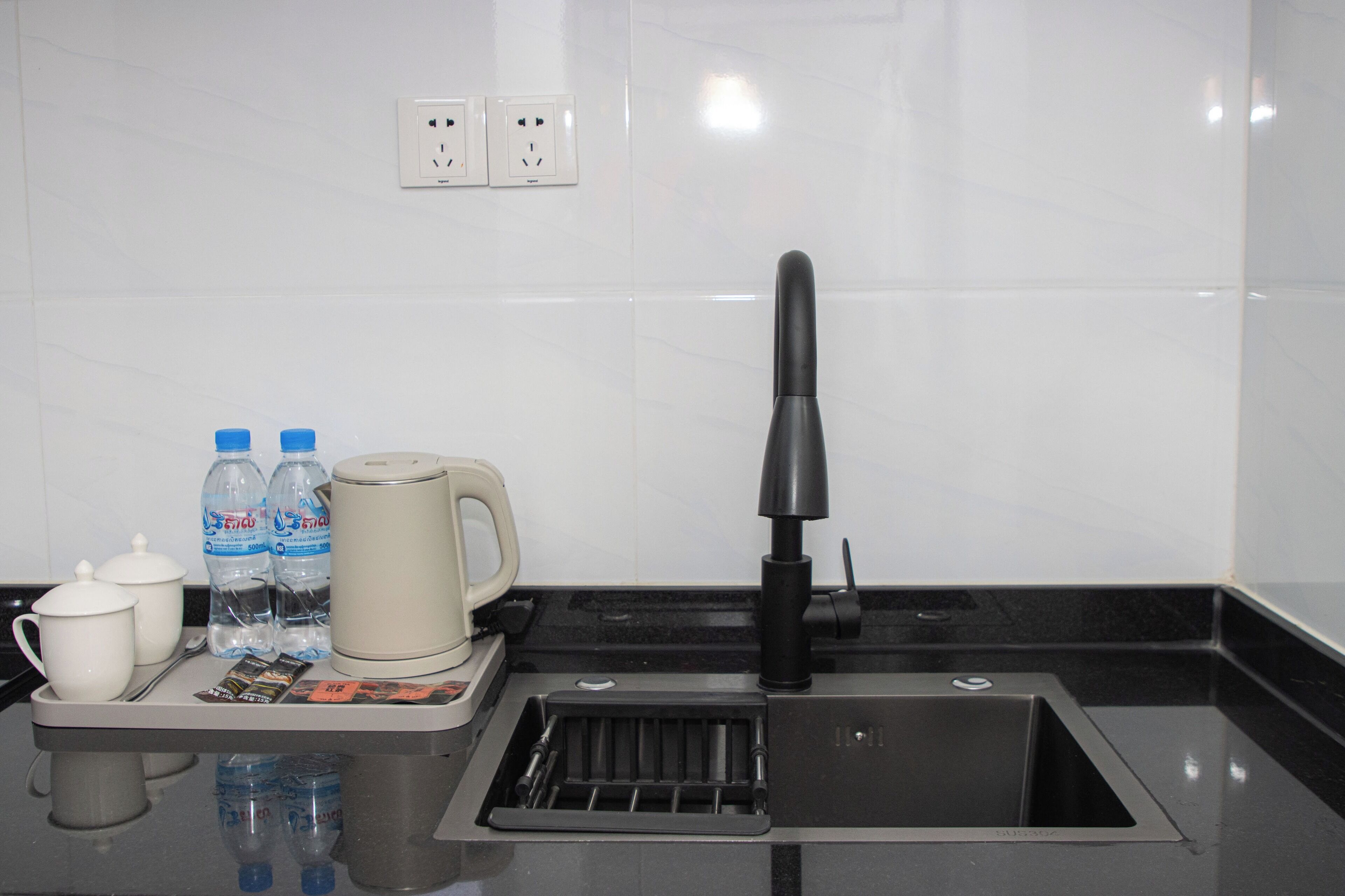 Une cuisine moderne avec un évier noir, une machine à café et deux bouteilles d’eau.