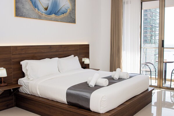 Une chambre d’hôtel moderne avec un grand lit, une tête de lit en bois, un tableau au mur et une vue sur le paysage urbain par la fenêtre.