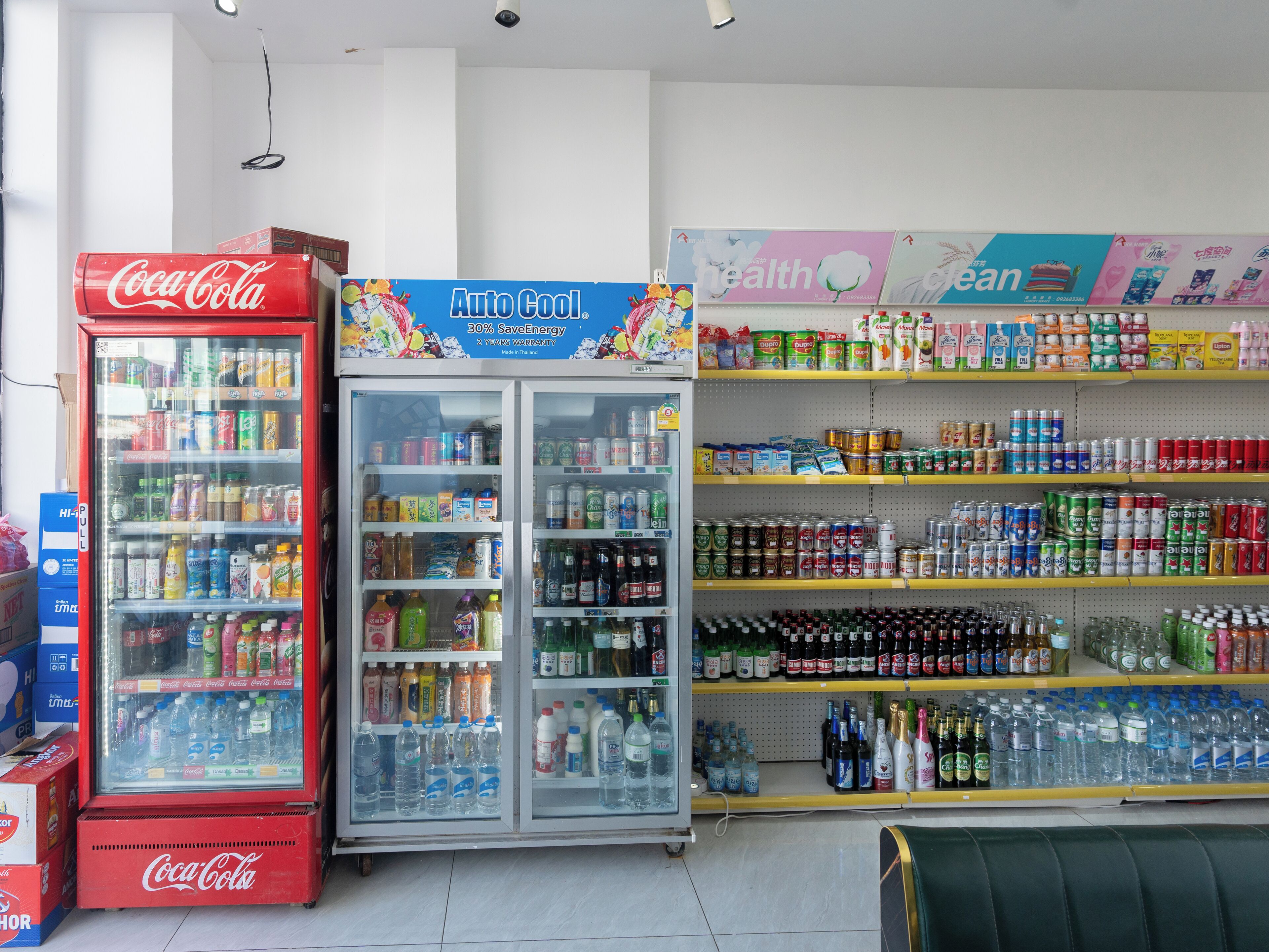 A store with a Coca-Cola refrigerator, an Auto Cool refrigerator, and shelves stocked with various beverages and snacks.