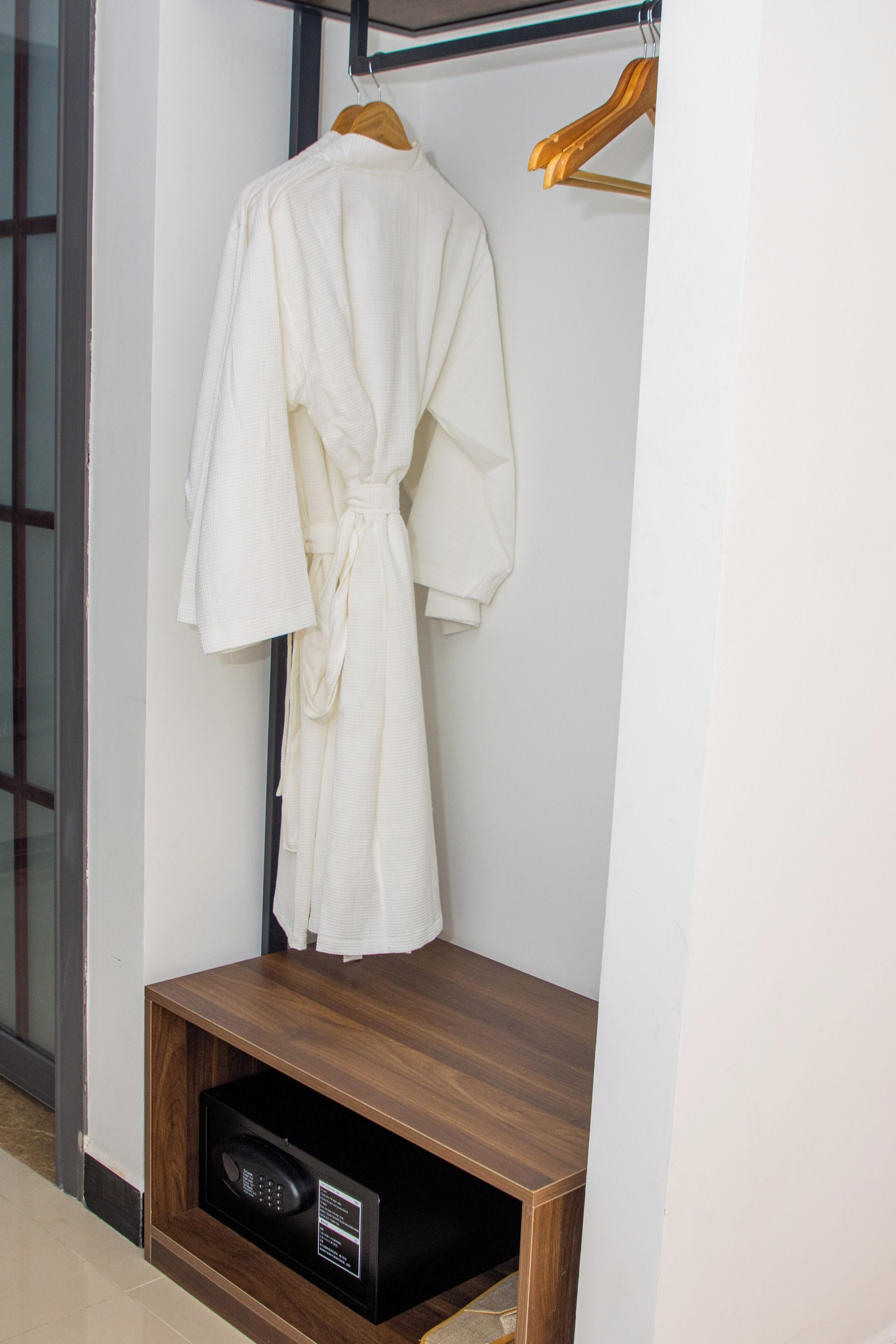 Een witte badjas hangt aan een houten kapstok in een hoek, met een houten plank eronder.