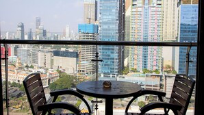 A balcony with a round table and two chairs, overlooking a cityscape with various buildings. - A One Oasis River View Hotel (Phnom Penh)