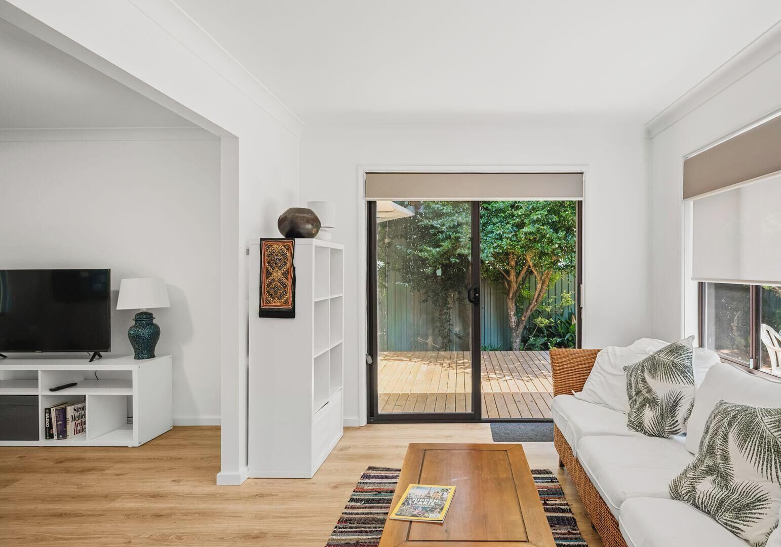 A modern living room with a TV, bookshelf, and a sofa with a view to a backyard.
