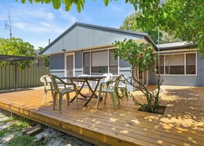 A modern house with a deck, a dining table with chairs, and a small tree.