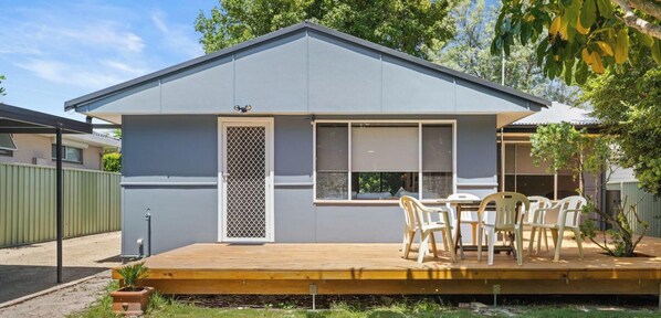 Een modern huis met een plat dak, een houten terras, een raam met zonwering en een deur met een lattenwerkdecor.
