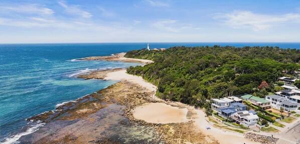 A coastal property with a beach, rocky shoreline, and a lighthouse in the distance.