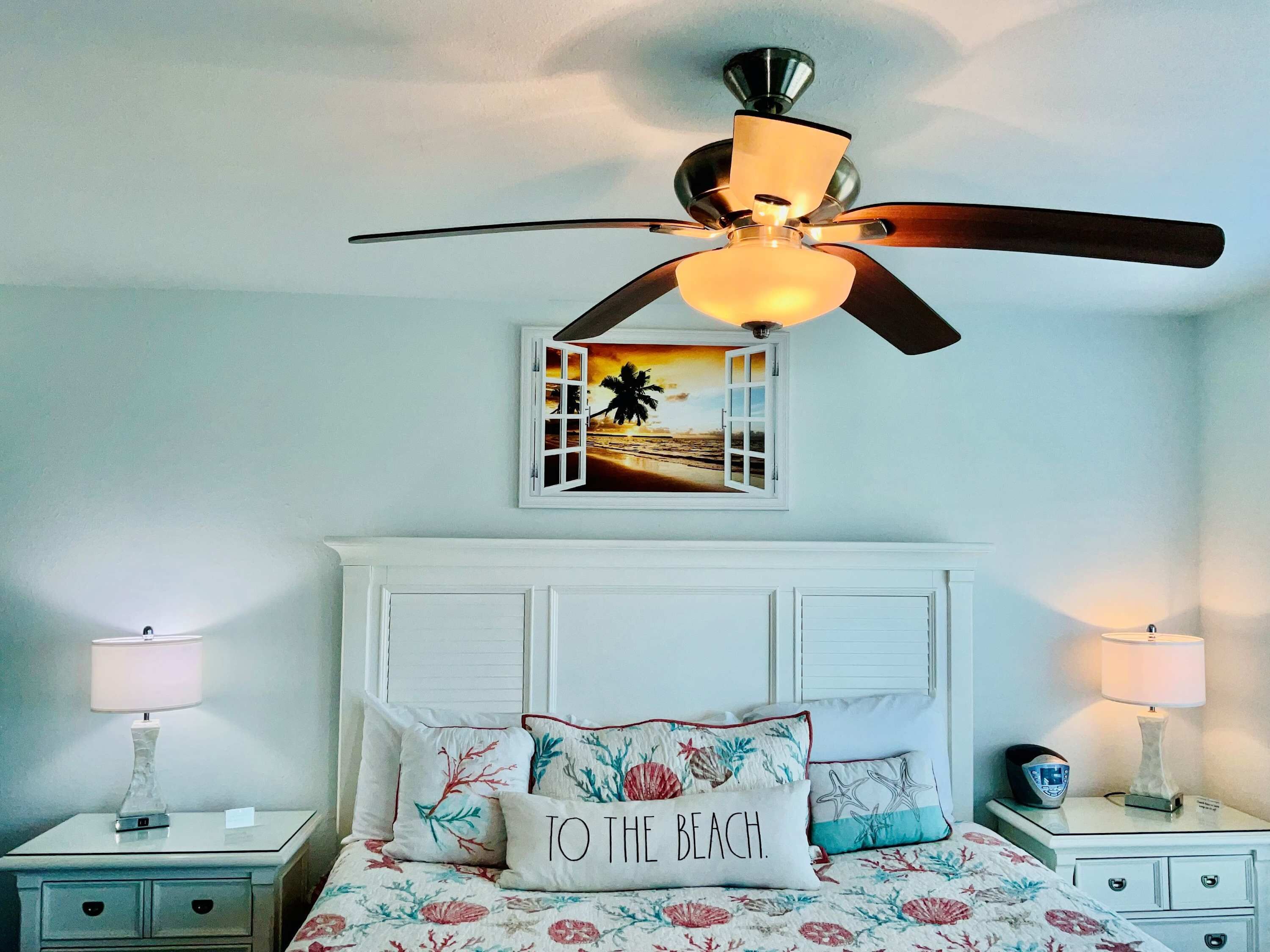 A bedroom with a bed, two bedside tables, a ceiling fan, and a wall-mounted picture.