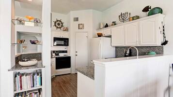 A kitchen with white cabinetry, a microwave, stove, and a sink. There are decorative items on shelves and a bookshelf.