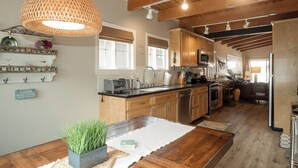 Een keuken met houten kastjes, een centraal eiland, een hanglamp en een eethoek met een tafel en stoelen.