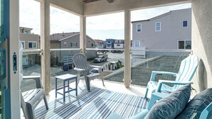 Een balkon met uitzicht op omliggende huizen, een overdekt terras met stoelen en een tafel, en een gebouw met een schuin dak.
