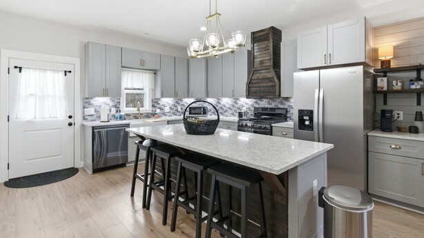 A modern kitchen with a central island, stainless steel appliances, and a wooden accent wall. - The Bella - Modern Equestrian Home with Park Views near Weatherford Square! (Weatherford)