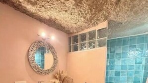 Un baño con un espejo redondo, un lavabo, un mueble de madera y una zona de ducha con azulejos azules.
