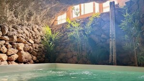 Un área de spa con pared de piedra, una pequeña cascada y plantas tropicales.