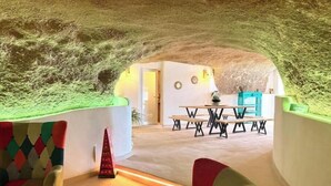 Una habitación subterránea con una mesa, sillas, un objeto rojo con forma de cono y sillas de colores.
