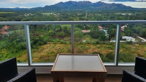 Un balcon avec une table et des chaises, offrant une vue sur un paysage montagneux verdoyant, parsemé de bâtiments.