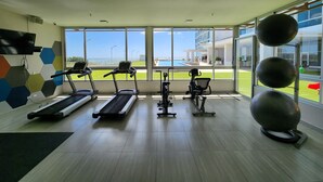 Une salle de sport équipée de tapis de course, de vélos d’appartement et de ballons d’exercice, avec de grandes fenêtres donnant sur une piscine et des bâtiments.