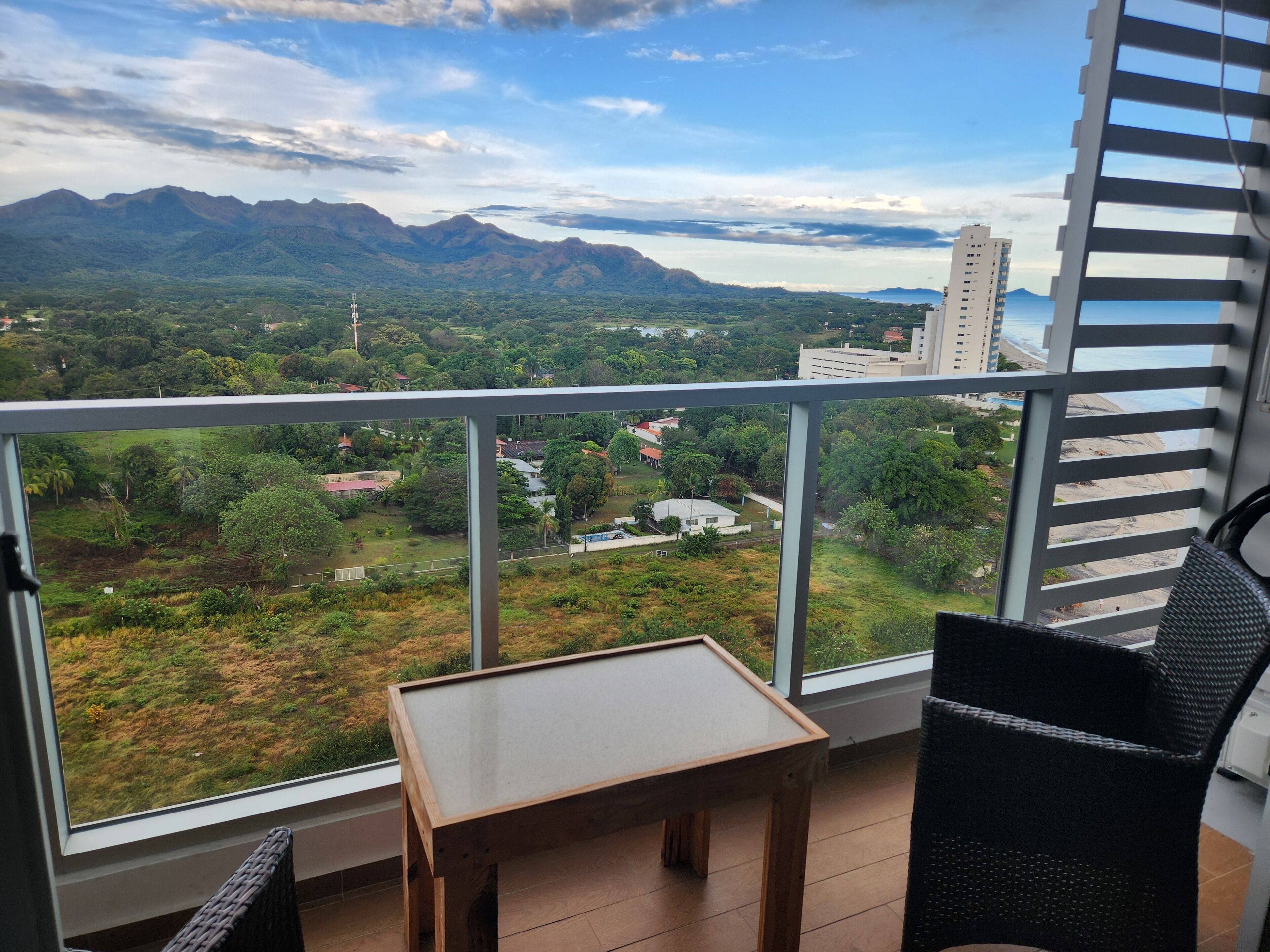 A balcony with a view of a mountainous landscape, a small table, and a wicker chair.