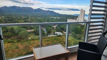 A balcony with a view of a mountainous landscape, a small table, and a wicker chair.