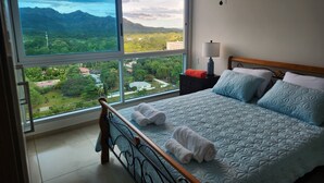 Une chambre avec une grande fenêtre, un lit avec une literie bleue et une table de chevet avec une lampe.