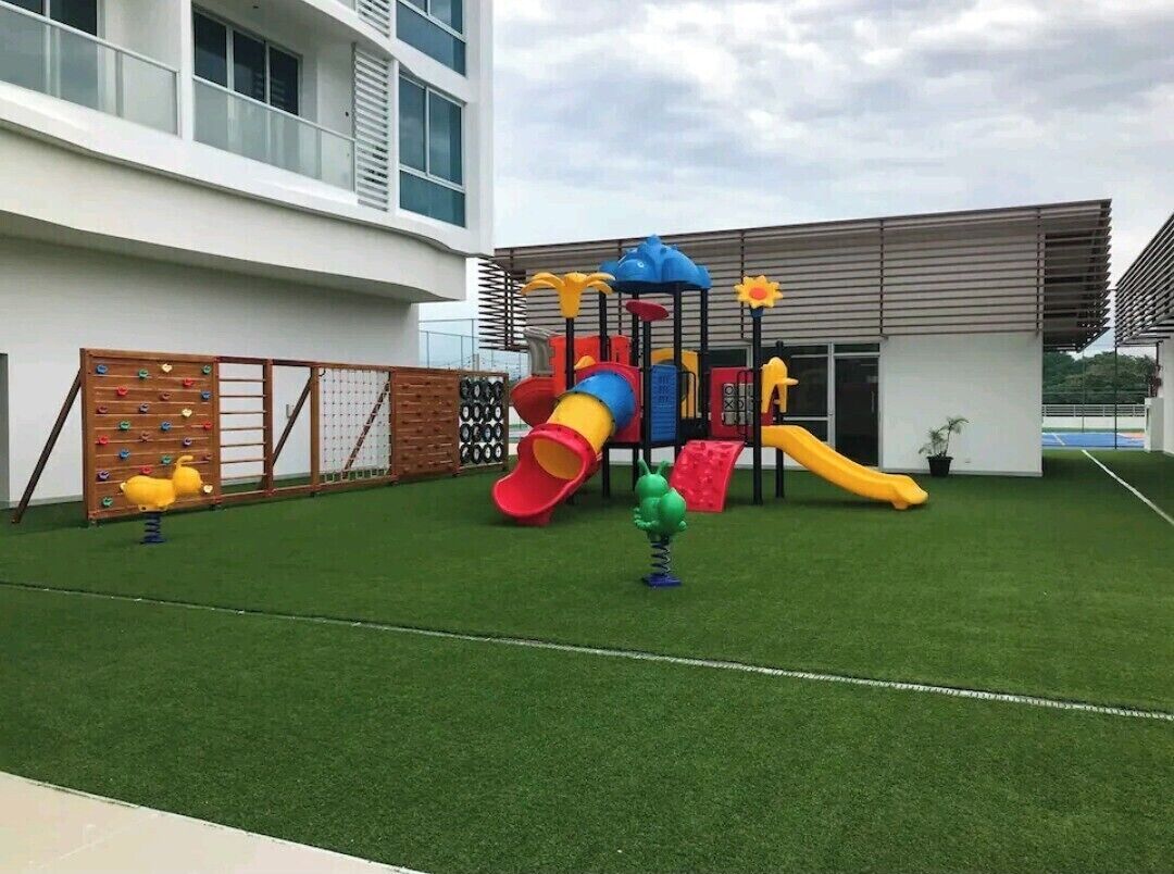 A playground with slides and climbing structures, surrounded by a fenced area and a building in the background.