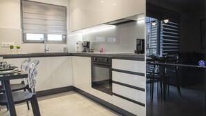 A modern kitchen with a black countertop, stainless steel appliances, and a dining area with a glass table and chairs. - Black & White 2BR Apt steps from Mavili Square (Athina)