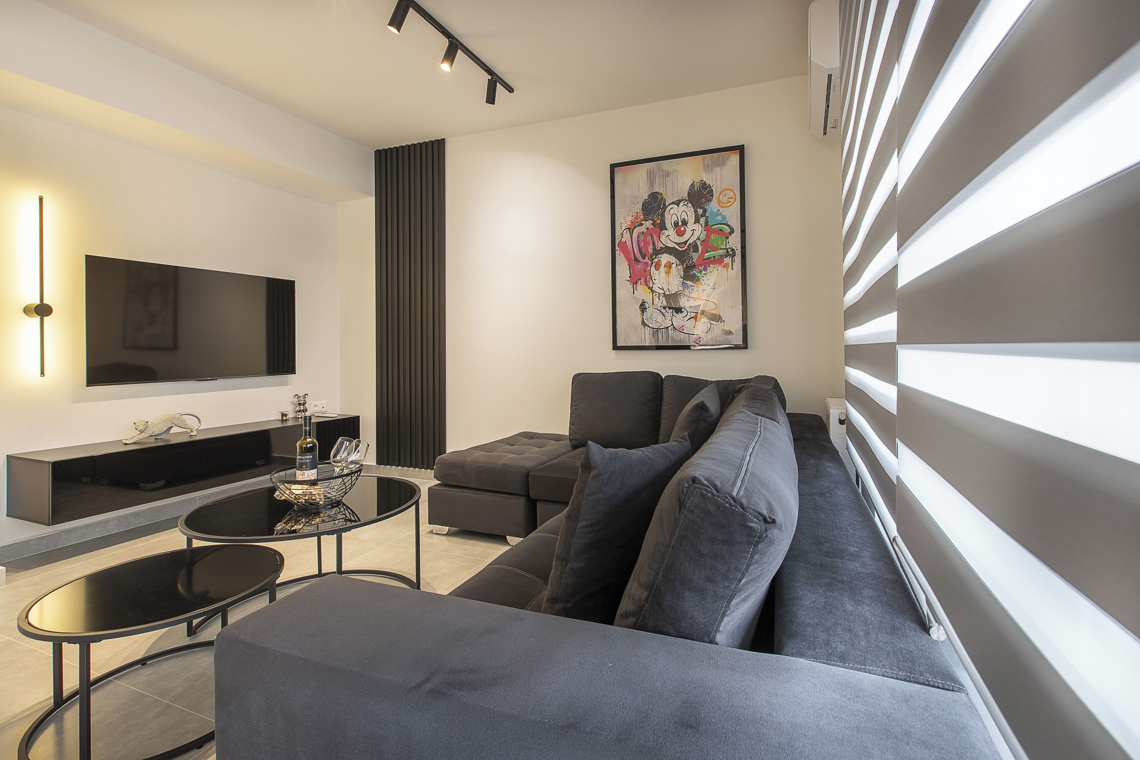 A modern living room with a large flat-screen TV, a dark-colored sofa, a coffee table, and a decorative wall piece.