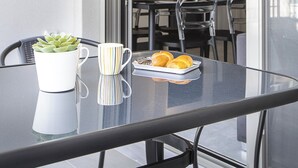 A modern dining area with a glass table, chairs, a potted plant, a striped mug, and a plate with pastries. - Black & White 2BR Apt steps from Mavili Square (Athina)