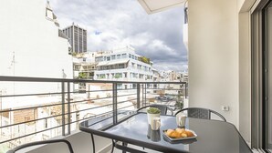 A balcony with a glass table, chairs, a potted plant, and a tray of pastries. - Black & White 2BR Apt steps from Mavili Square (Athina)