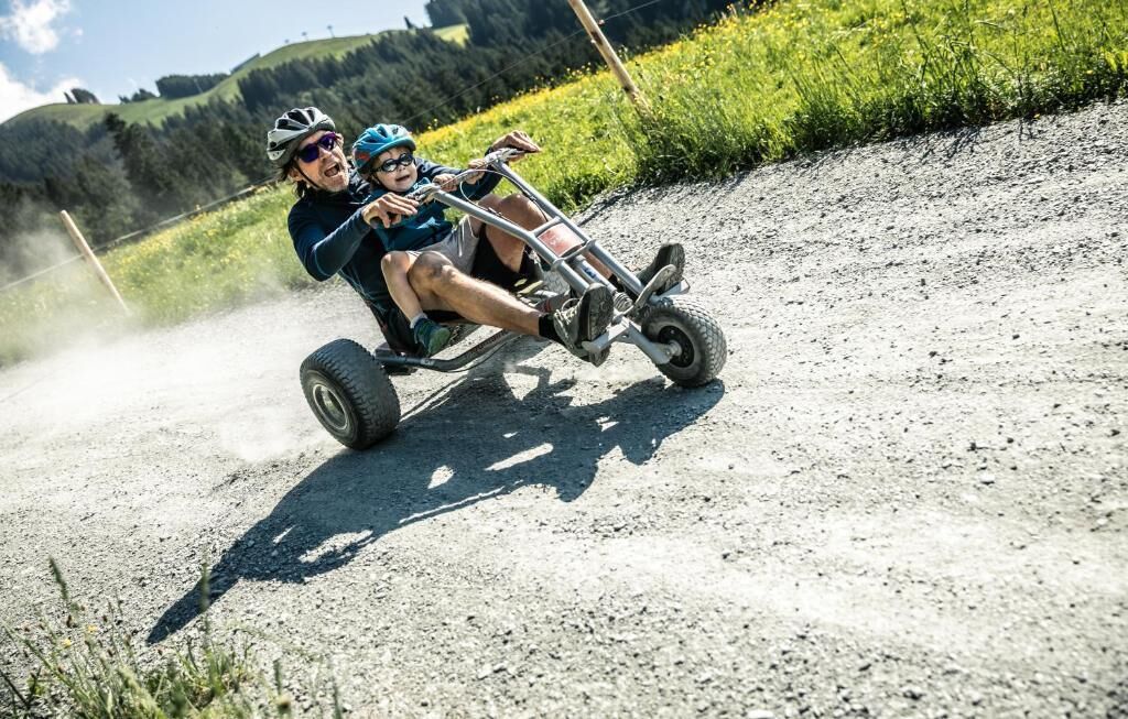 A person riding a three-wheeled vehicle on a dirt road with a hilly landscape in the background.