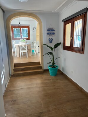 Ein Flur mit Holzboden, einem Blumentopf und einer Treppe, die in einen Essbereich mit weißen Stühlen und einem Tisch führt.