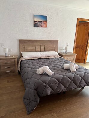 Ein Schlafzimmer mit einem hölzernen Kopfteil, einem großen Bett mit gesteppter Bettdecke, zwei Nachttischen mit Lampen und einer Holztür.
