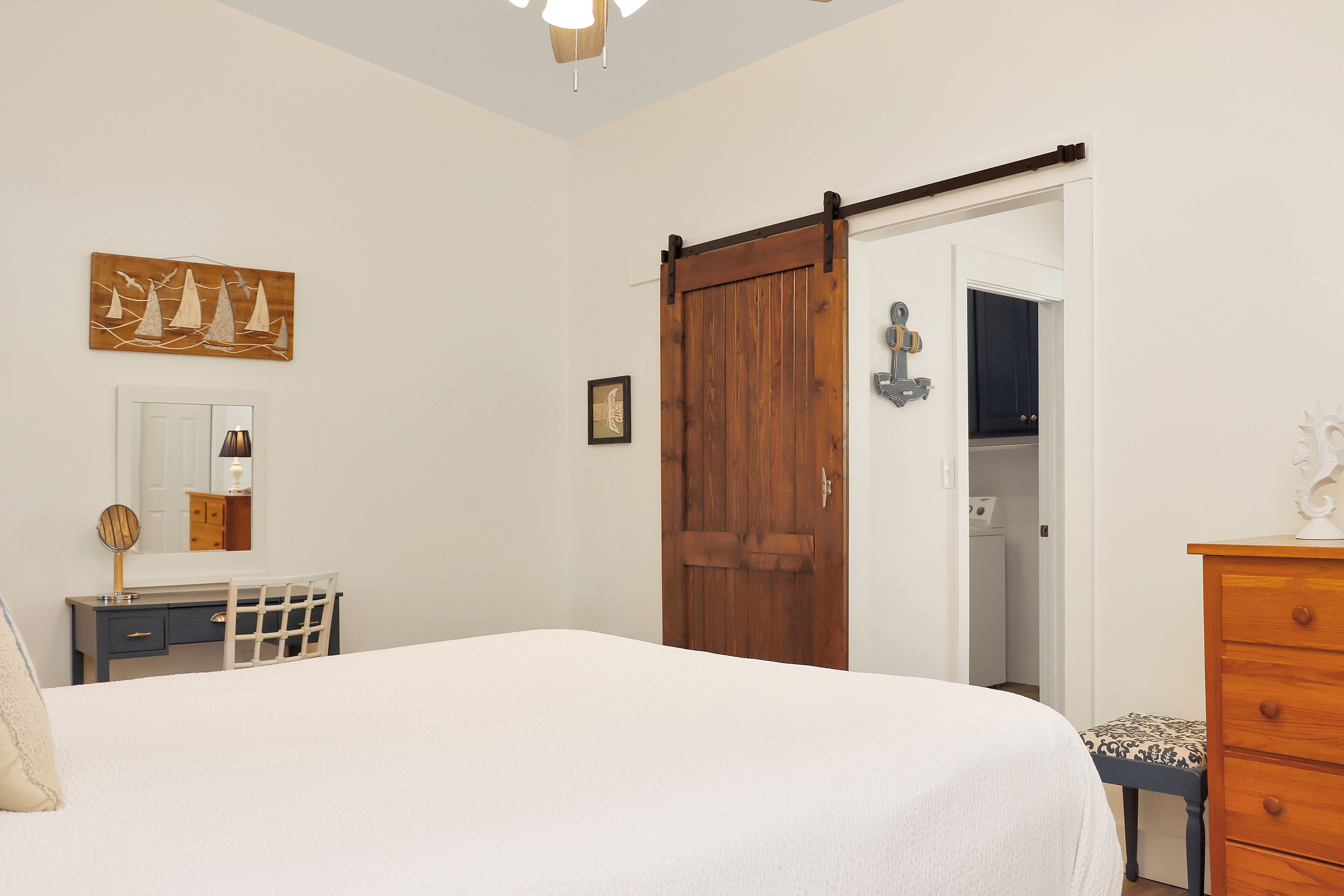 Ein Schlafzimmer mit Bett, Kommode, Spiegel, einer Tür und einem an der Wand befestigten Kunstwerk.
