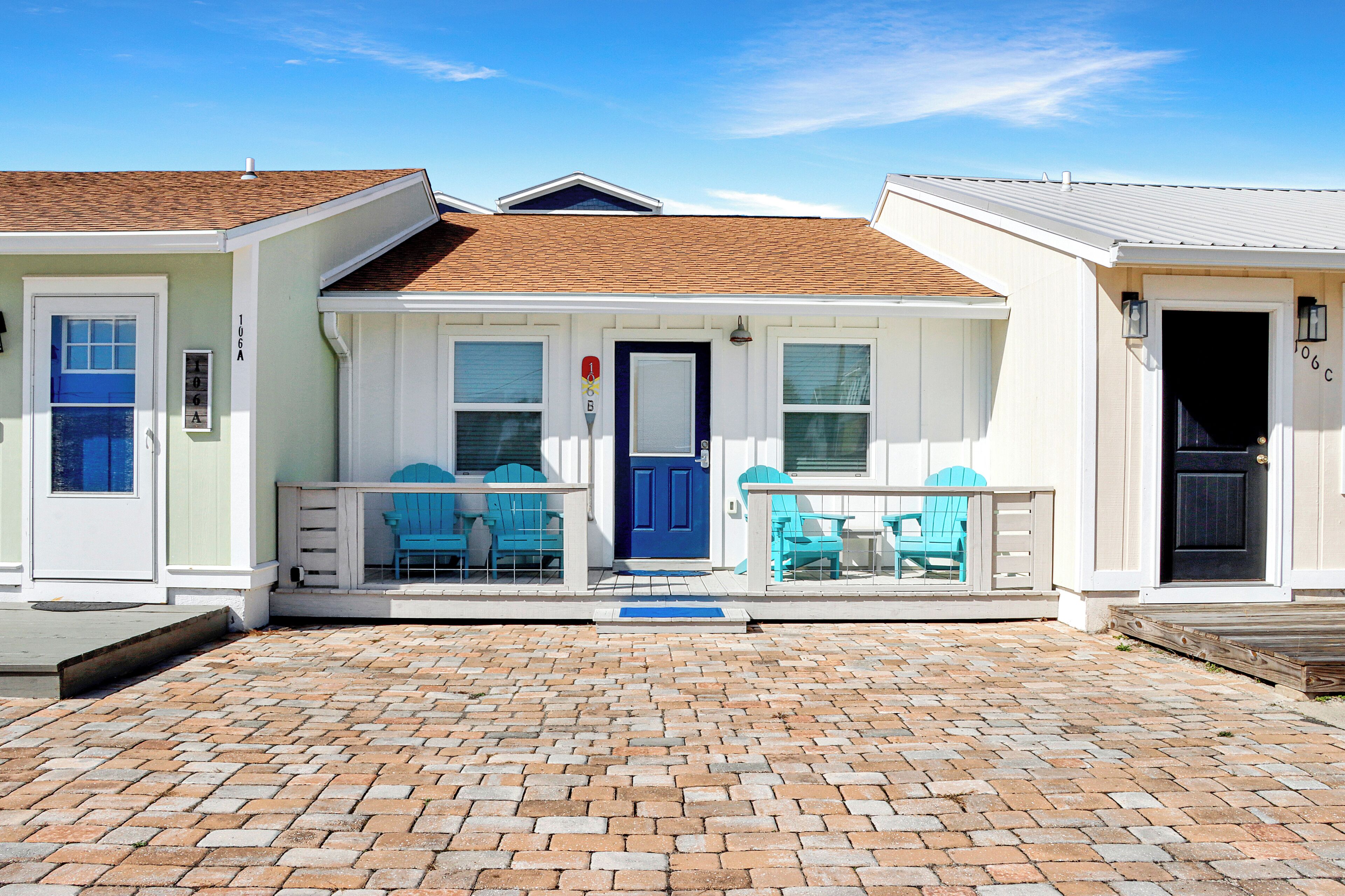 Une maison à deux étages avec un porche à l’avant, une porte bleue et une allée pavée en briques.