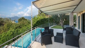 Un balcon aménagé avec du mobilier d’extérieur, une piscine et une vue sur la mer et les montagnes.