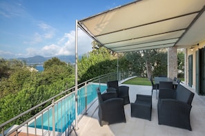 Ein Balkon mit Gartenmöbeln, ein Pool und Blick auf das Meer und die Berge.