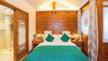 Una habitación de hotel con cabecera de madera, una cama con ropa de cama verde, dos mesitas de noche con lámparas y un ventanal con cortinas.