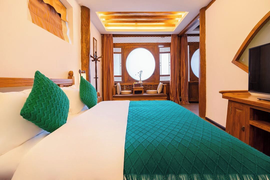 A hotel room with a large bed, a TV, and a view of the outside through a window.