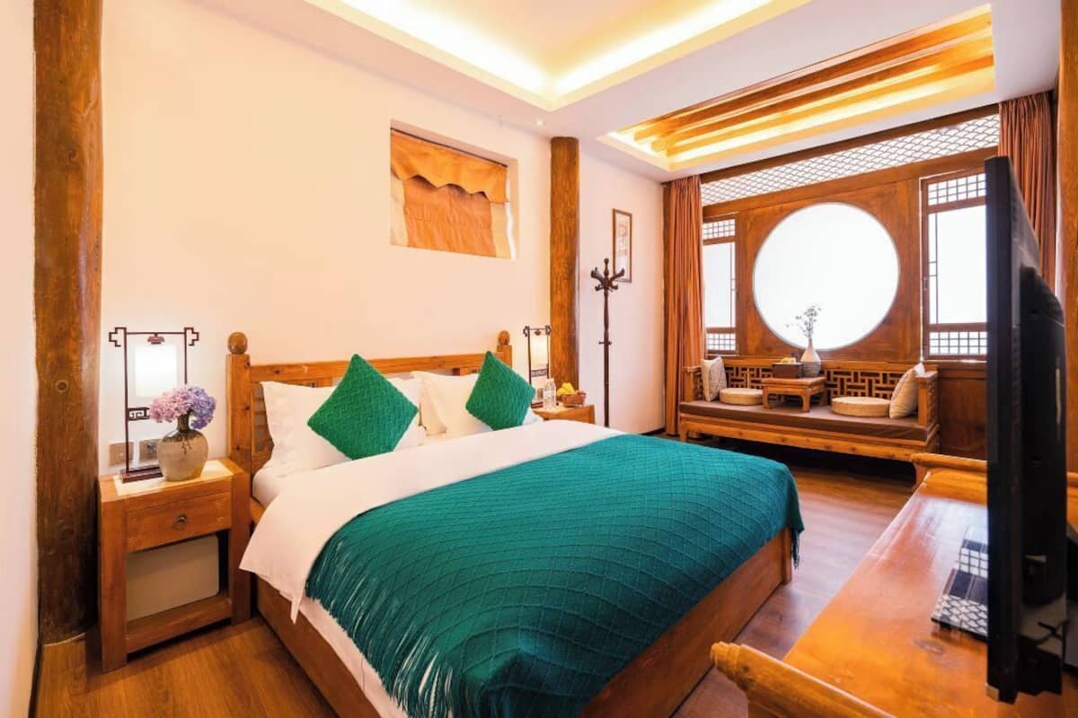 A traditional-style bedroom with a wooden bed, green bedding, and a wooden bench with cushions.
