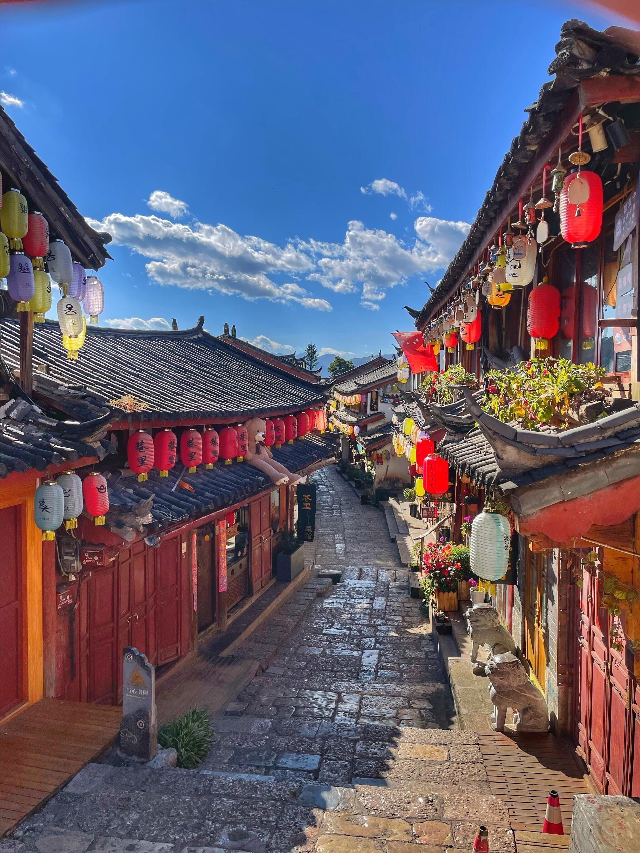 A narrow street with traditional architecture, red lanterns, and stone paving.