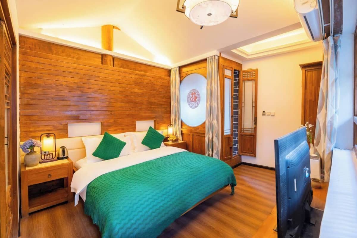 A hotel room with a wooden headboard, a bed with green bedding, a bedside table with a lamp, and a television.