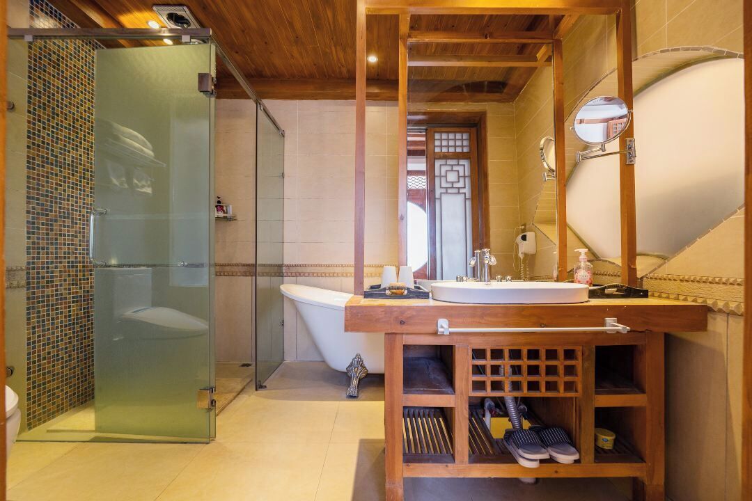 Un baño con cabina de ducha de vidrio, una bañera independiente, un tocador de madera con lavabo y un zapatero empotrado.