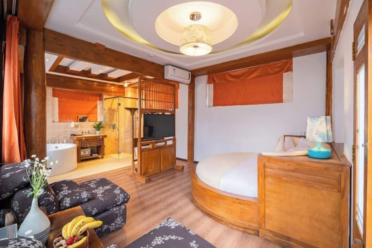 A compact living space with a round bed, a television, a wooden cabinet, and a small kitchenette.