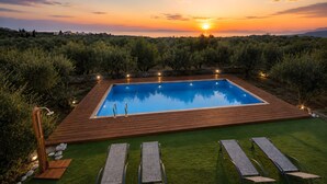 Piscina rectangular con muelle de madera, rodeada de vegetación y vistas al atardecer.
