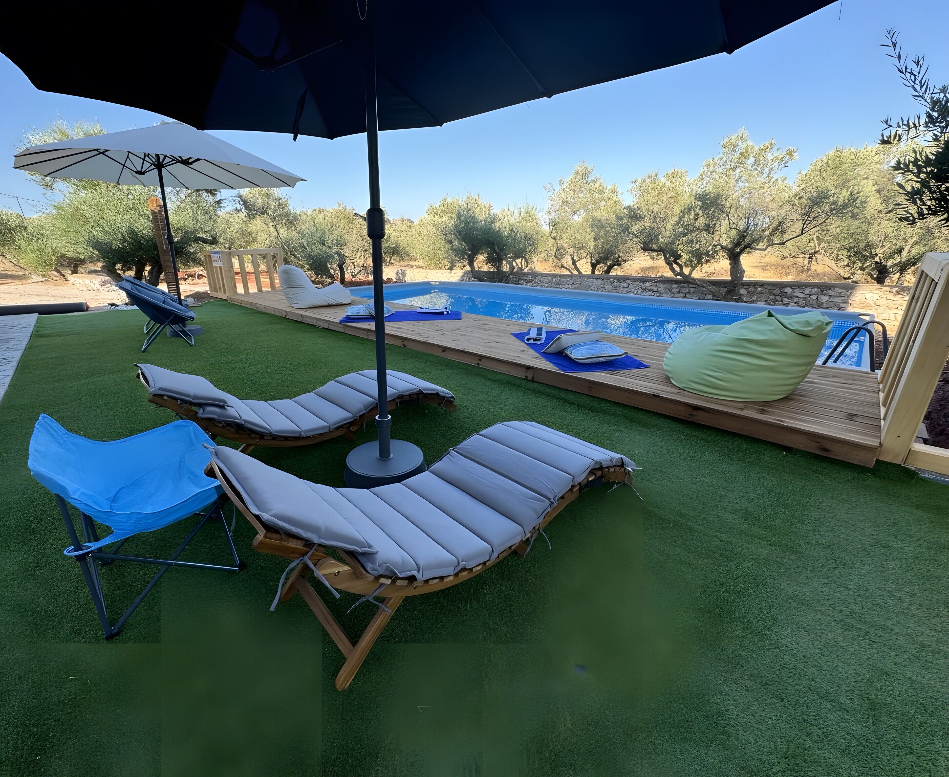 Ein Poolbereich mit Liegestühlen, einem blauen Sonnenschirm und einer Holzterrasse.