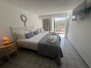 Une chambre à coucher avec un lit, une table de chevet, une lampe et une vue sur l’extérieur.