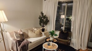 A living room with a sofa, a chair, a small round table with a plant, and a window with curtains.