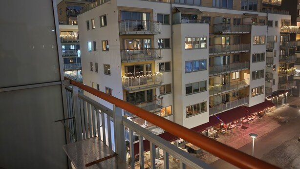 A multi-story residential building with balconies, a ground-level restaurant, and a view of the street below.
