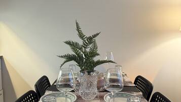 A dining table set for four with clear glassware, a decorative fern, and patterned tablecloth.